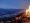 Feuer im rechten Teil des Bildes, Abend und Blick auf die Lichter einer Stadt im Tal