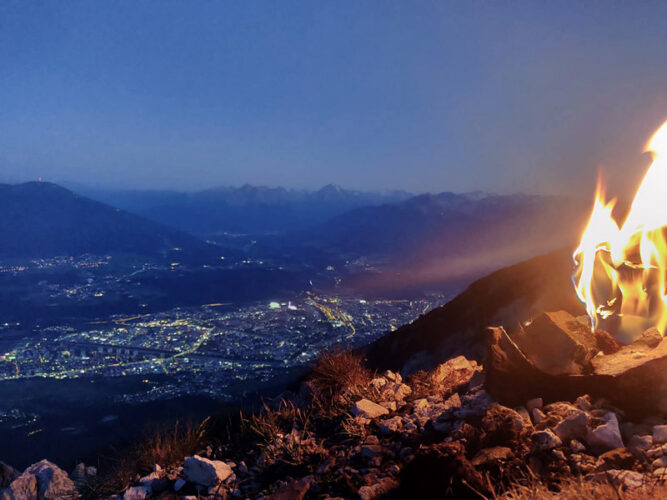 Feuer im rechten Teil des Bildes, Abend und Blick auf die Lichter einer Stadt im Tal