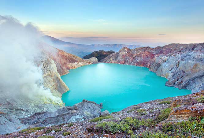 Ein türkisfarbener Kratersee am Fuße des Vulkans mit der blauen Lava.