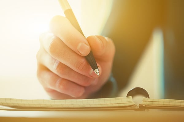 Hand mit Stift über einem aufgeschlagenen Notizbuch