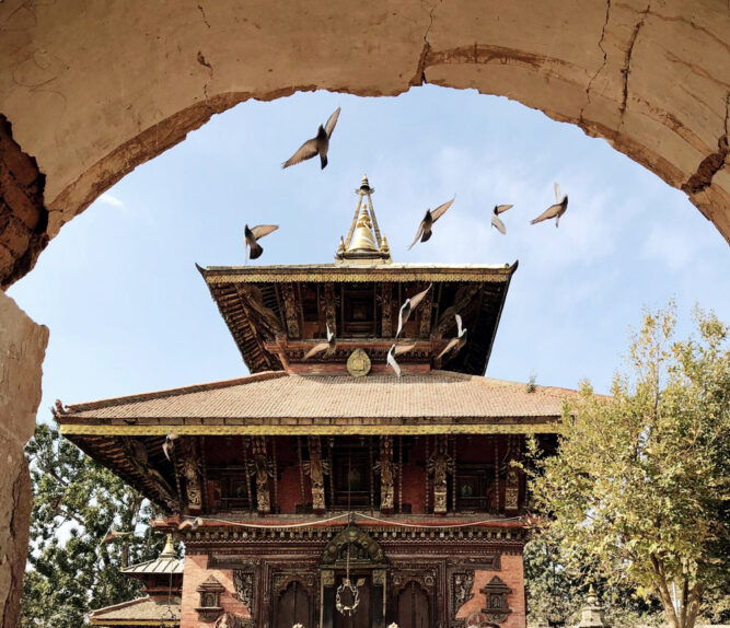 Blick durch einen Torbogen auf einen Tempel. Tauben fliegen in der Luft.