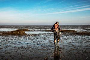 Ein Mann mit Gummistiefeln geht über schlammigen Boden am Wattenmeer