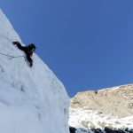 Eiskletterer an senkrechter Eiswand. Gebirge im Hintergrund.