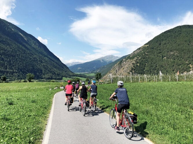 Gruppe mit Fahrrädern fährt durch Wiesen in Tal, Vinschgau.