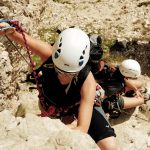 Eine Frau mit Kletterhelm Elios beim Klettern an einem Klettersteig. ©unsplash