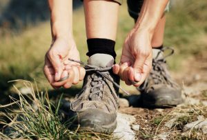 Zwei Frauenhände beim Schnüren von Trekkingschuhen