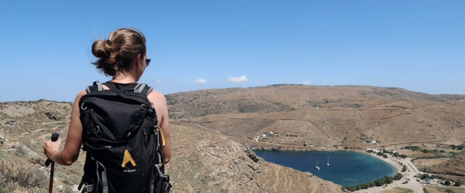 Wanderin von hinten, blickt hinunter auf einen See. Hügeliges Gelände