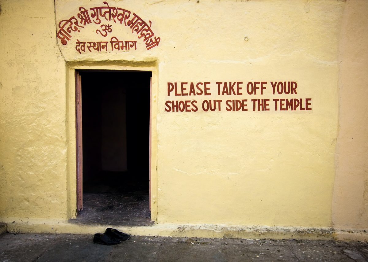 Ein paar Schuhe vor einem Tempel in Indien mit der Aufschrift "Bitte Schuhe ausziehen".