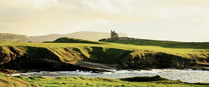 Küste und grüne Wiesen mit einer Burg in Irland