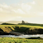 Küste und grüne Wiesen mit einer Burg in Irland