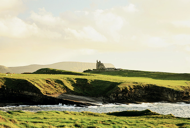 Küste und grüne Wiesen mit einer Burg in Irland