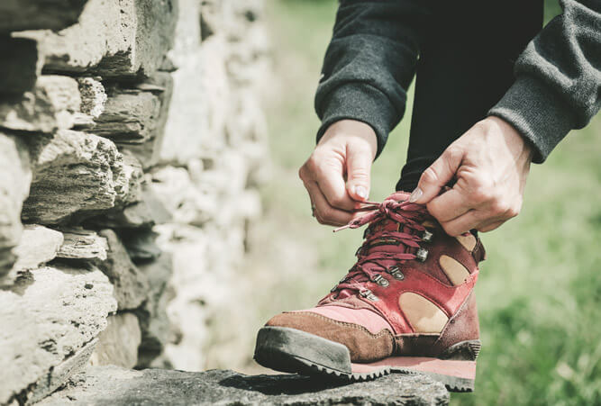 Hände einer Frau, die während einer Wanderung ihre Schuhe auf einen Stein schnürt