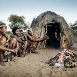 Drei afrikanische Stammesleute vor einer Strohhütte