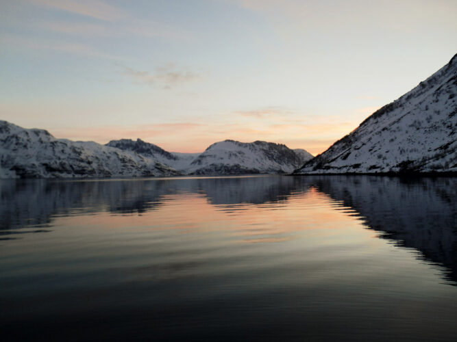 Himmel kurz nach Sonnenuntergang an Meeresbucht, schwarzes Wasser und verschneite Berge