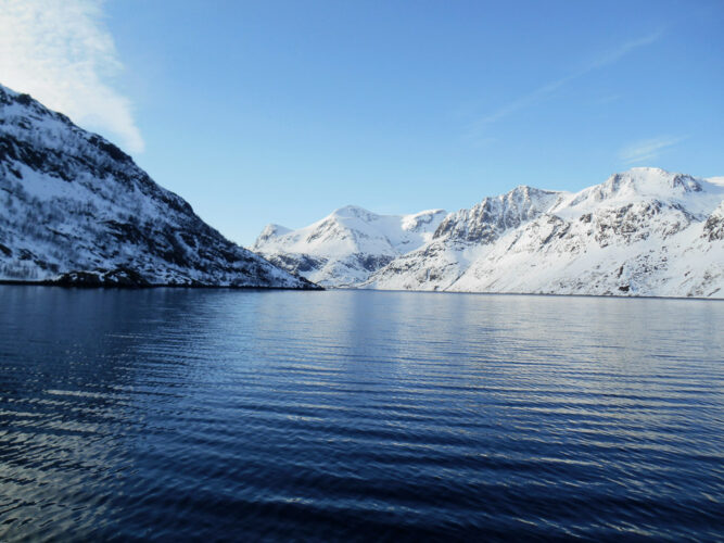 Dunkelblaues Wasser umgeben von verschneiten Bergen, klarer Himmel