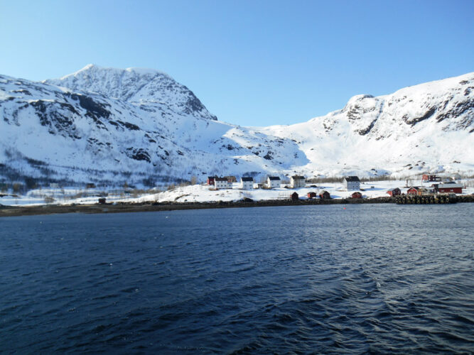 Dunkles Wasser, im Hintergrund verschneite Berge, Häuser in der Bucht