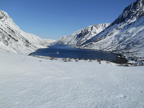 Eine verschneite Meeresbucht, dunkelblaues Wasser, wolkenloser Himmel