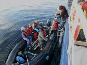 Mehrere Personen geben Rucksäcke und Skier in ein schwarzes Schlauchboot