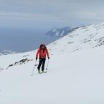 Skitourengeher mit roter Jacke geht auf Kamera zu, Himmel wolkenbehangen