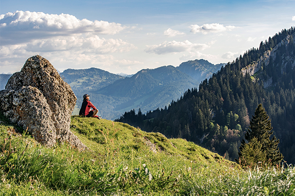 frau mit roter jacke sitzt auf almwiese