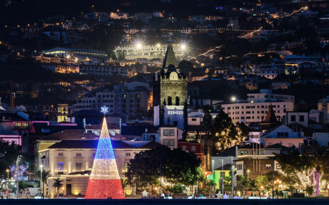 Bunt leuchtende Stadt. Ein Weihnachtsbaum aus roten, weißen und blauen Lichtern. In der Mitte ein Kirchturm.