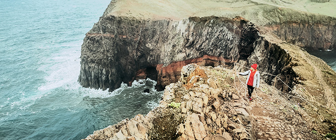 Wanderin mit roter Mütze und rotem Pulli an der Küste von Ponta de São Lourenço im Osten von Madeira, Portugal
