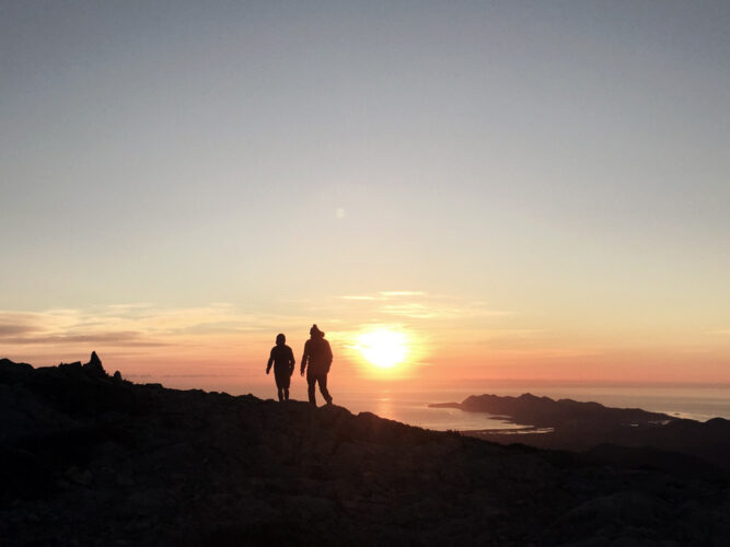 Sonnenuntergang auf einem Berg, roter Himmel und schwarze Umrisse, Silhouetten zweier Wanderer