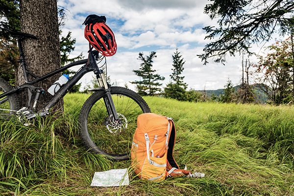 Fahrrad mit rotem Helm und orangenem Rucksack an einem Baum