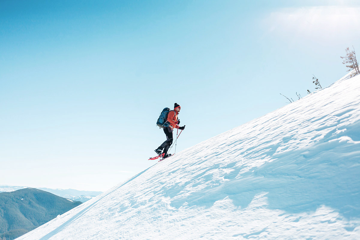 Mann auf Schneeschuhen erklimmt mit Schnee bedeckten Berg