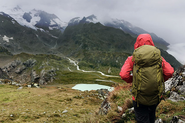 Wanderin in roter Regenjacke mit Rucksack blickt auf nebelverhangene Berge und einen See