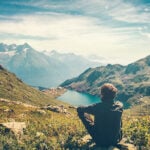 Auf Stein sitzender Mann mit Blick auf einen Bergsee