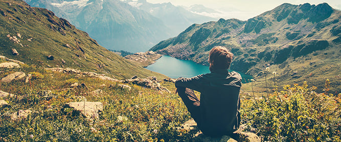 Auf Stein sitzender Mann mit Blick auf einen Bergsee