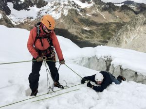 Mann mit roter alpiner Ausrüstung zieht Mann aus Gletscherspalte.