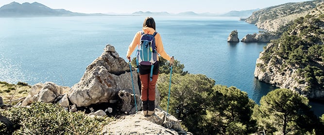 Wanderin mit Trekkingstöcken an einer Klippe bei Formentor auf Mallorca