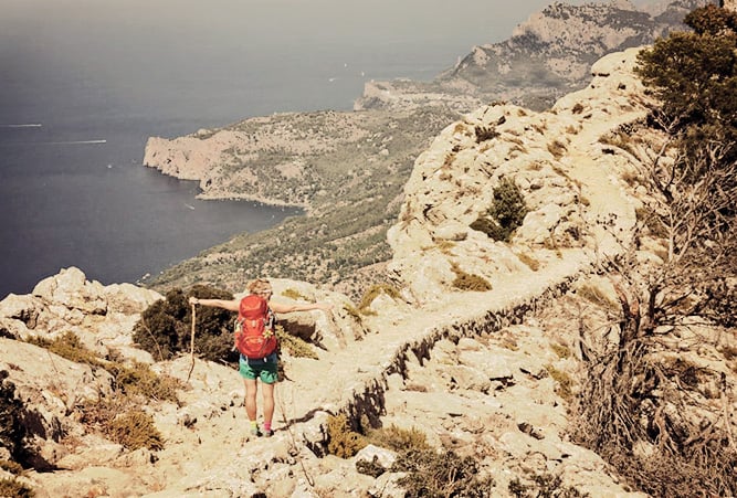 Wanderin mit ausgestreckten Armen an der Küste auf dem GR221 auf Mallorca
