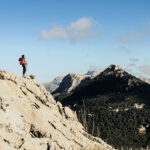 Wanderin mit Trekkingstöcken auf einem Berggipfel mit Blick auf den Puig de l Ofre auf Mallorca