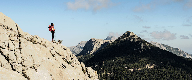 Wanderin mit Trekkingstöcken auf einem Berggipfel mit Blick auf den Puig de l Ofre auf Mallorca