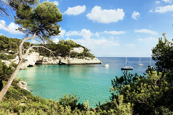 Cala Mitjana auf Menorca mit blauem Wasser und Booten