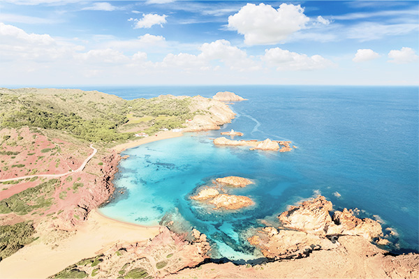 Blick auf die Cala Pregonda mit roten Felsklippen auf Menorca, Spanien