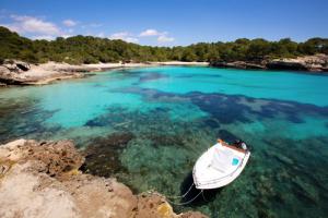 Türkisblaue Bucht, niedriges Wasser sodass man Algen erkennen kann, ein weißes Boot liegt im Vordergrund vor Anker, im Hintergrund ein Strand mit Wald dahinter