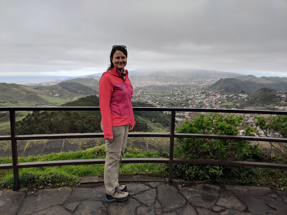 portraitfoto von frau in pinker jacke, hügelige landschaft im hintergrund