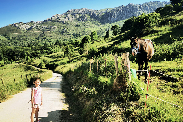 Mädchen auf einem Weg neben einer Wiese mit einem Pferd vor Bergpanorama in Spanien