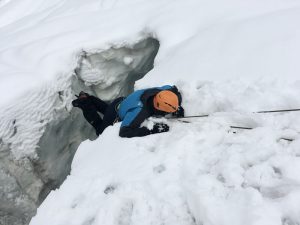 Mann mit blauer alpinen Ausrüstung wird an Seil aus Gletscherspalte gezogen.