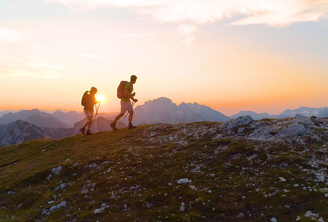 Zwei Bergsteiger gehen mit Wanderstöcken bergauf.