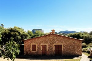 Steinerne Hütte umgeben von grünen Bäumen, blauer Himmel