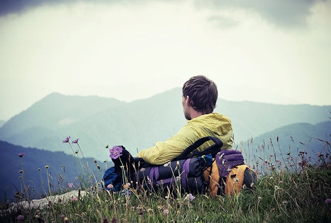 Wanderer macht auf einer Wiese Pause und blickt auf die Berge