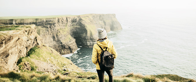 Frau vob hinten blickt auf Klippen in Irland