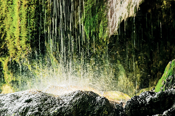 Wasser tropft auf Stein vor moosbehangenen Felswänden