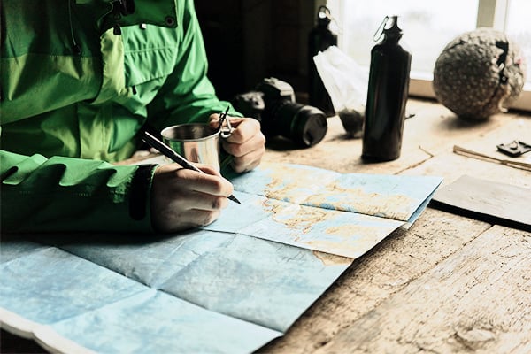 Mann in grünem Anorak mit Stift vor Weltkarte